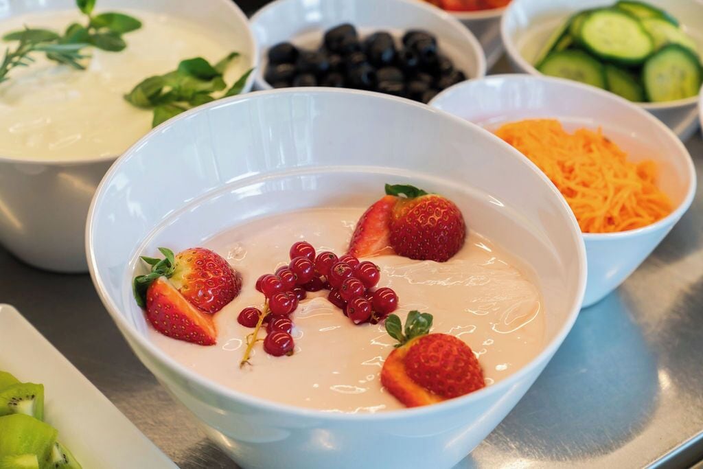 A variety of bowls containing different food items, including a bowl with a creamy dessert topped with strawberries and red currants.