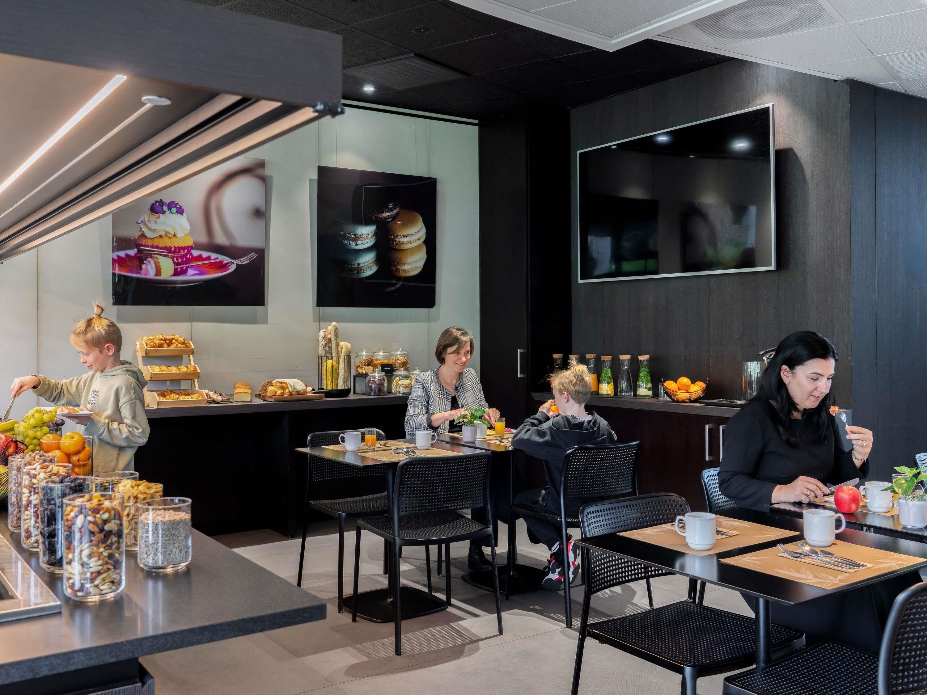 Un café moderno con mesas y sillas, una barra con productos alimenticios y un televisor montado en la pared.