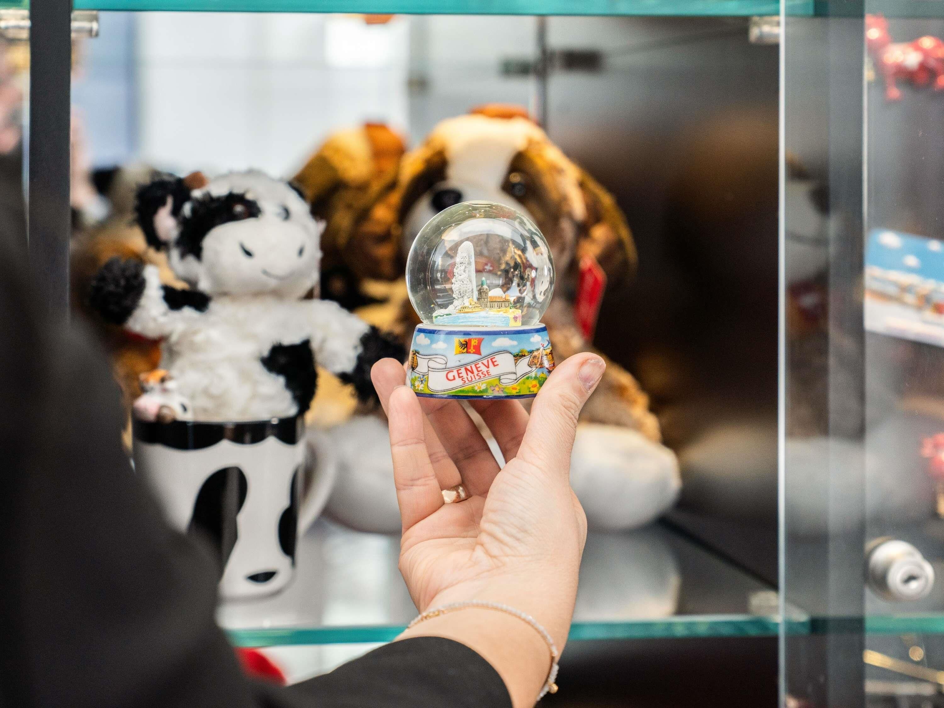 A hand holding a snow globe with a label that reads 'GENEVE SUISSE.'