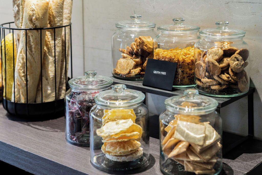 A display of gluten-free snacks in glass jars, including cookies and pastries, on a wooden shelf.