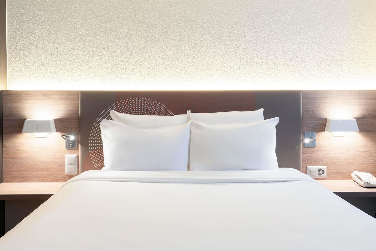 Une chambre d’hôtel avec un lit bien fait, deux lampes de chevet, un téléphone et un luminaire fixé au mur.