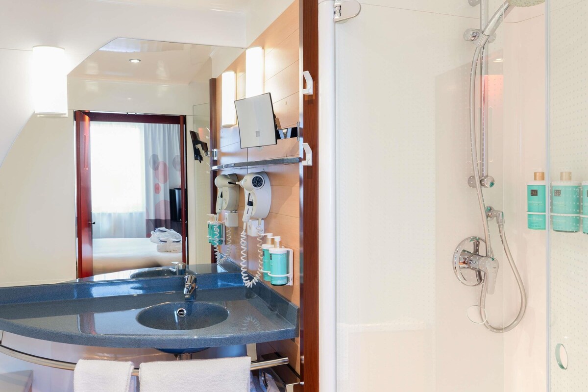 A hotel bathroom with a glass sink, a handheld showerhead, and a mirror.