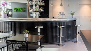 Zona de bar moderna con una barra curva, lámparas colgantes y una variedad de botellas y vasos.