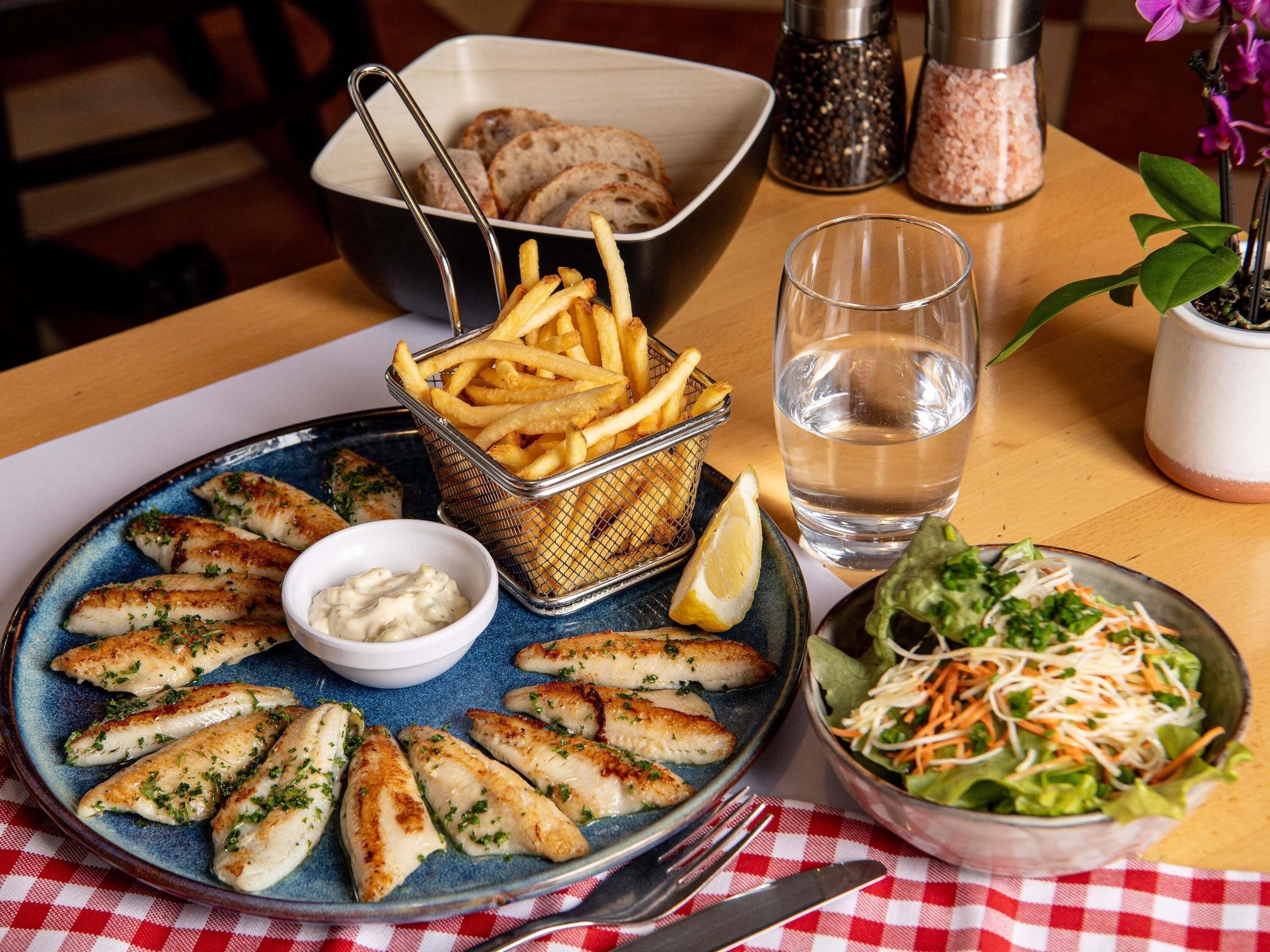 Un repas composé de poisson, de frites, de salade et de pain, servi sur une table.