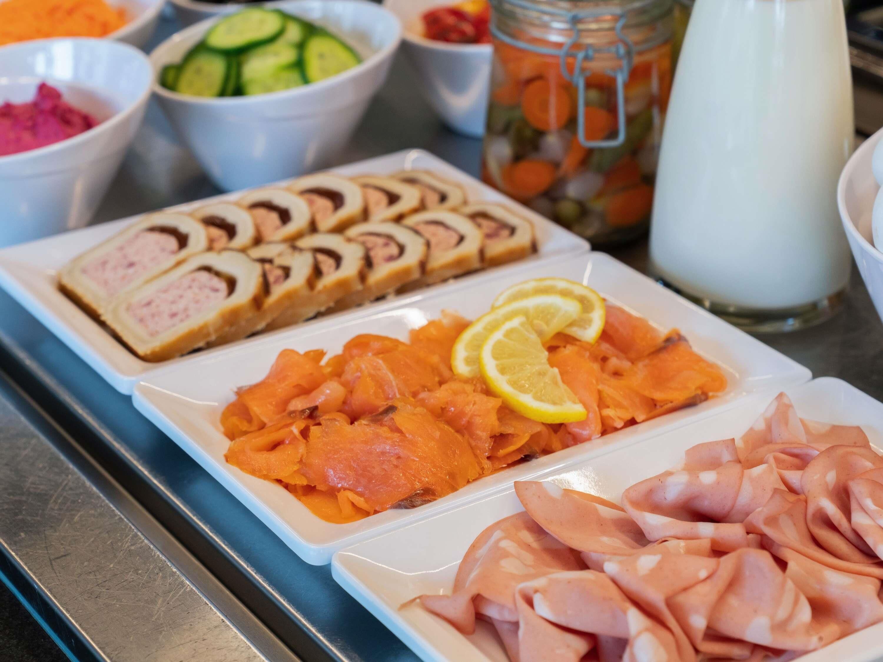 A buffet with various food items including sliced meat, smoked salmon, and pickled vegetables.