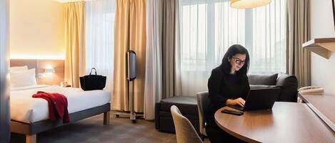 A hotel room with a bed, a desk, a laptop, and a chair.