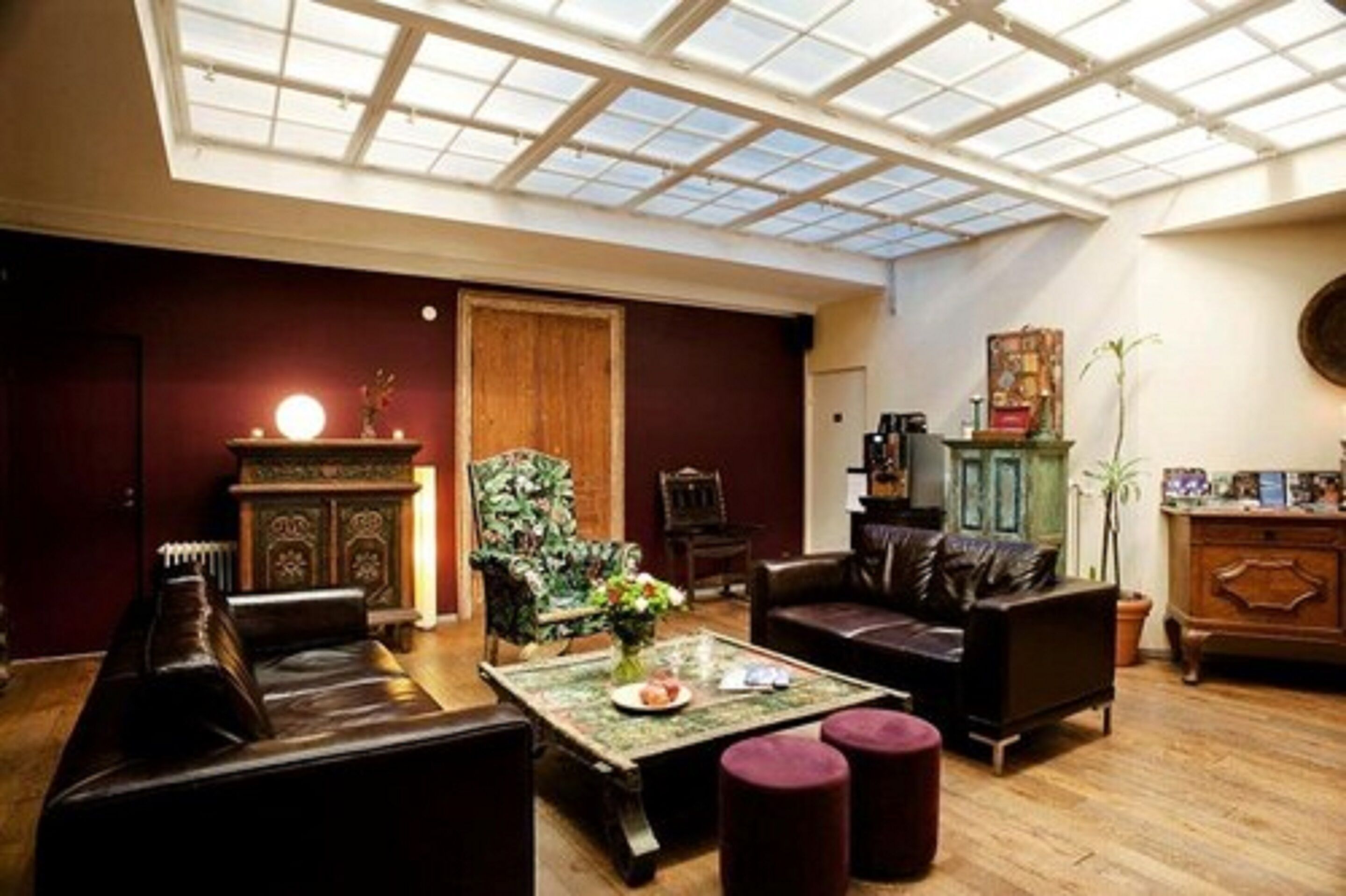 Een ruime woonkamer met een hoge plafond en dakraam, met leren banken, een houten kast en een salontafel.