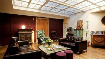 Een ruime woonkamer met een hoge plafond en dakraam, met leren banken, een houten kast en een salontafel.