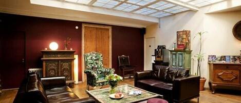 A spacious living room with a high ceiling and skylight, featuring leather sofas, a wooden cabinet, and a coffee table.