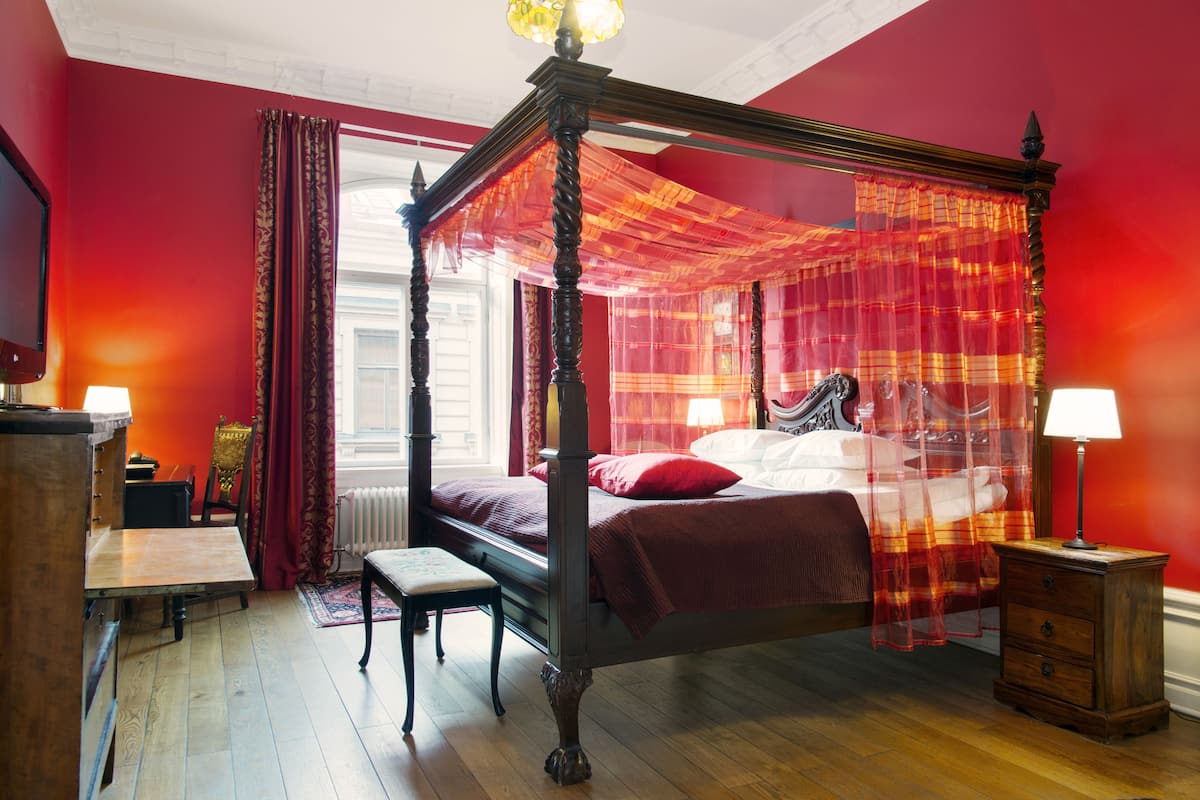 A four-poster bed with a canopy, a wooden nightstand, a bench, and a table with a lamp.