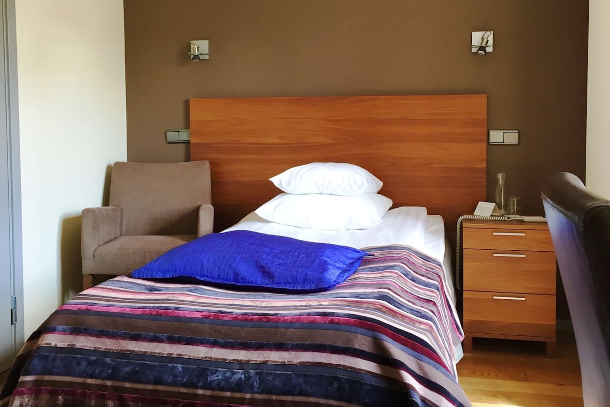 A single bed with a striped blanket, a wooden headboard, a bedside table with a lamp, and a chair.