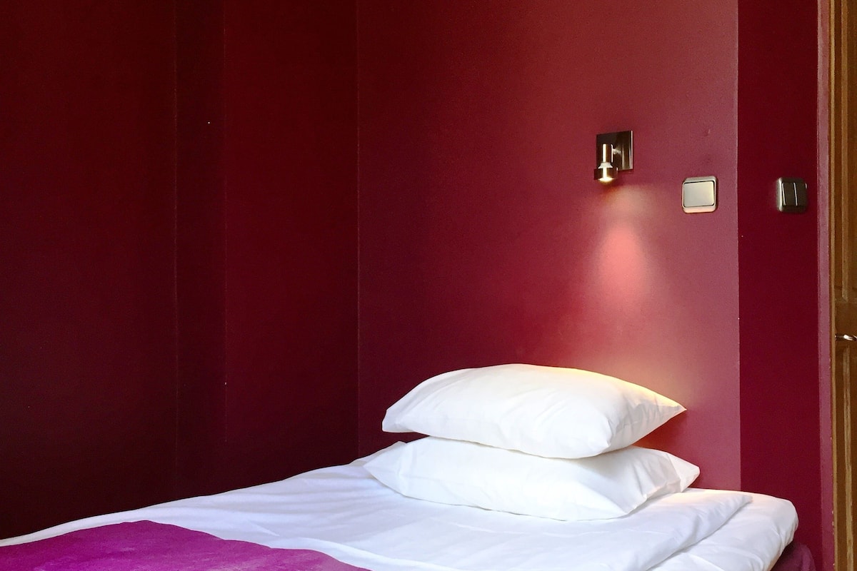 A single bed with white bedding and a purple throw blanket in a room with red walls.
