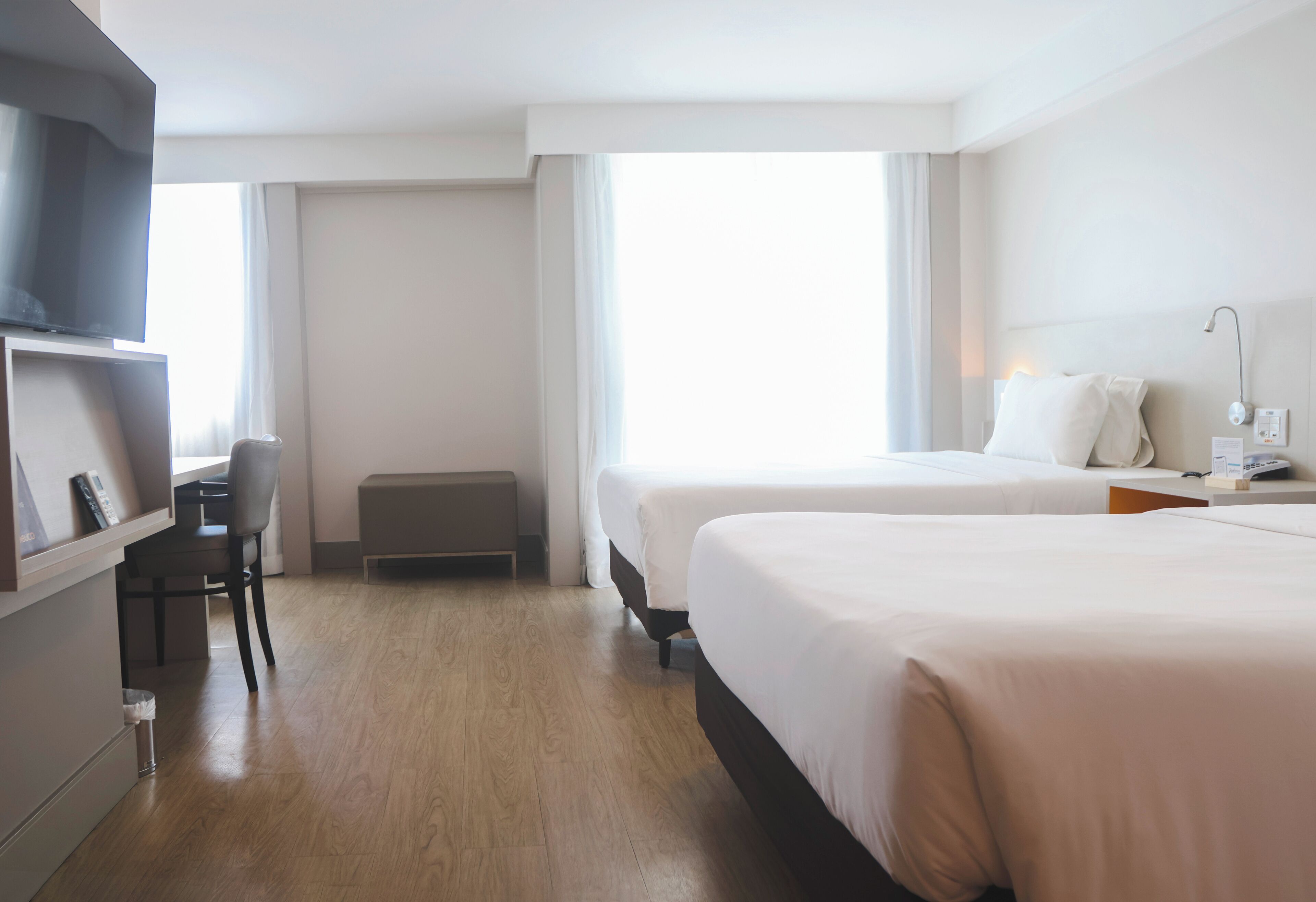 Habitación de hotel con dos camas, un escritorio, una silla, un televisor y una ventana con cortinas.