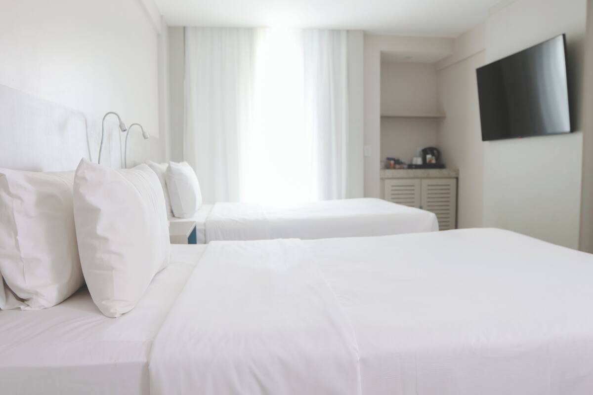 Ein Hotelzimmer mit zwei Betten, einem an der Wand befestigten Fernseher und einem Fenster mit Vorhängen.