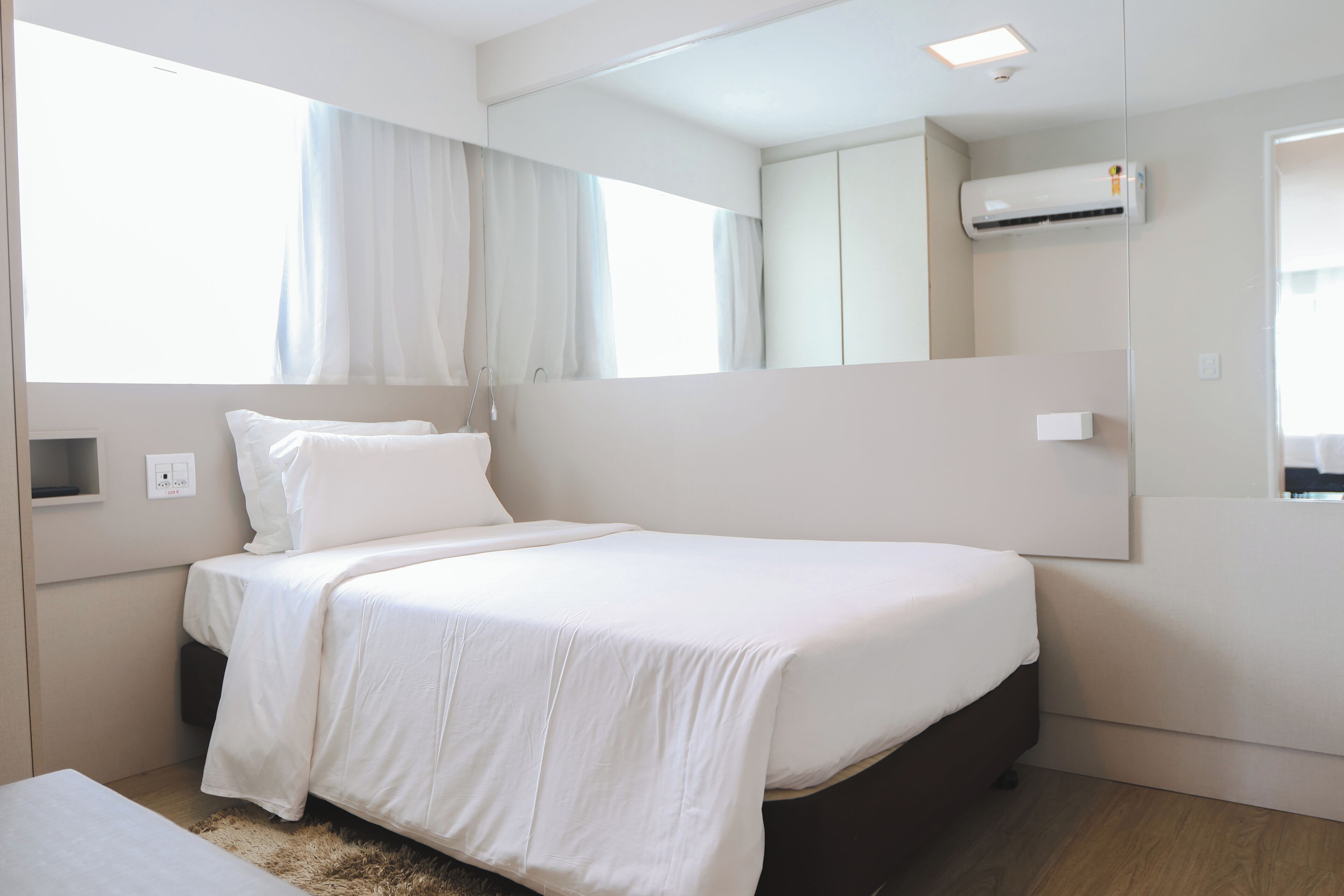 Habitación de hotel moderna con una cama grande, una mesita de noche, un espejo y un equipo de aire acondicionado.