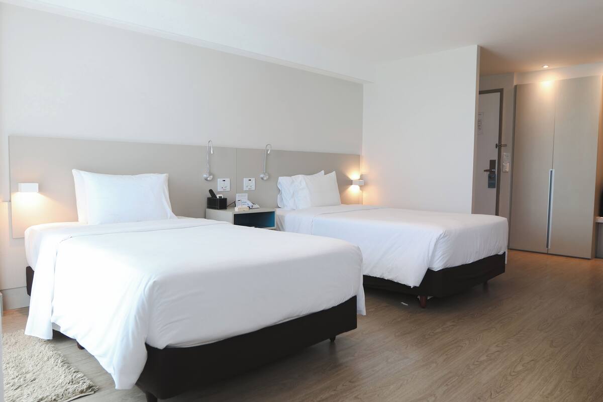 Ein Hotelzimmer mit zwei Betten, Holzboden und einer Tür.
