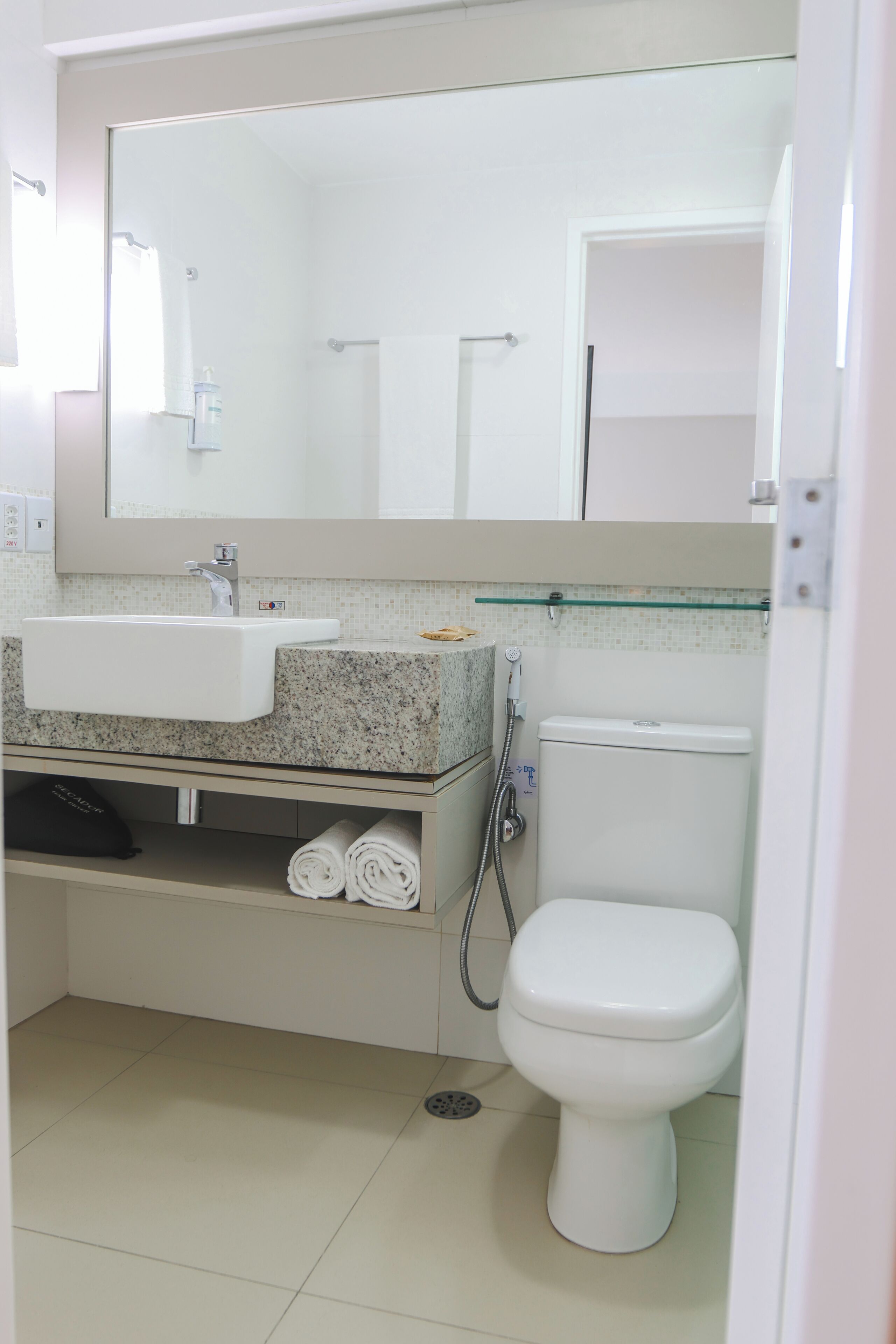 Un baño con un lavabo blanco, un espejo encima, un inodoro y una ducha.