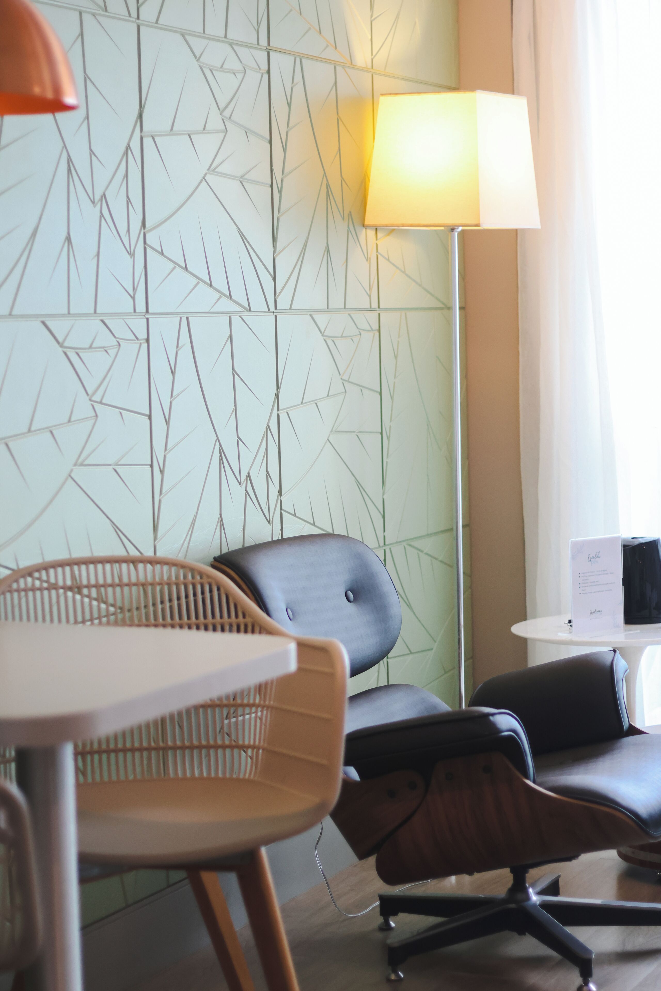 Uma cadeira de escritório moderna, uma mesa e uma luminária em um ambiente com papel de parede estampado com padrões geométricos.