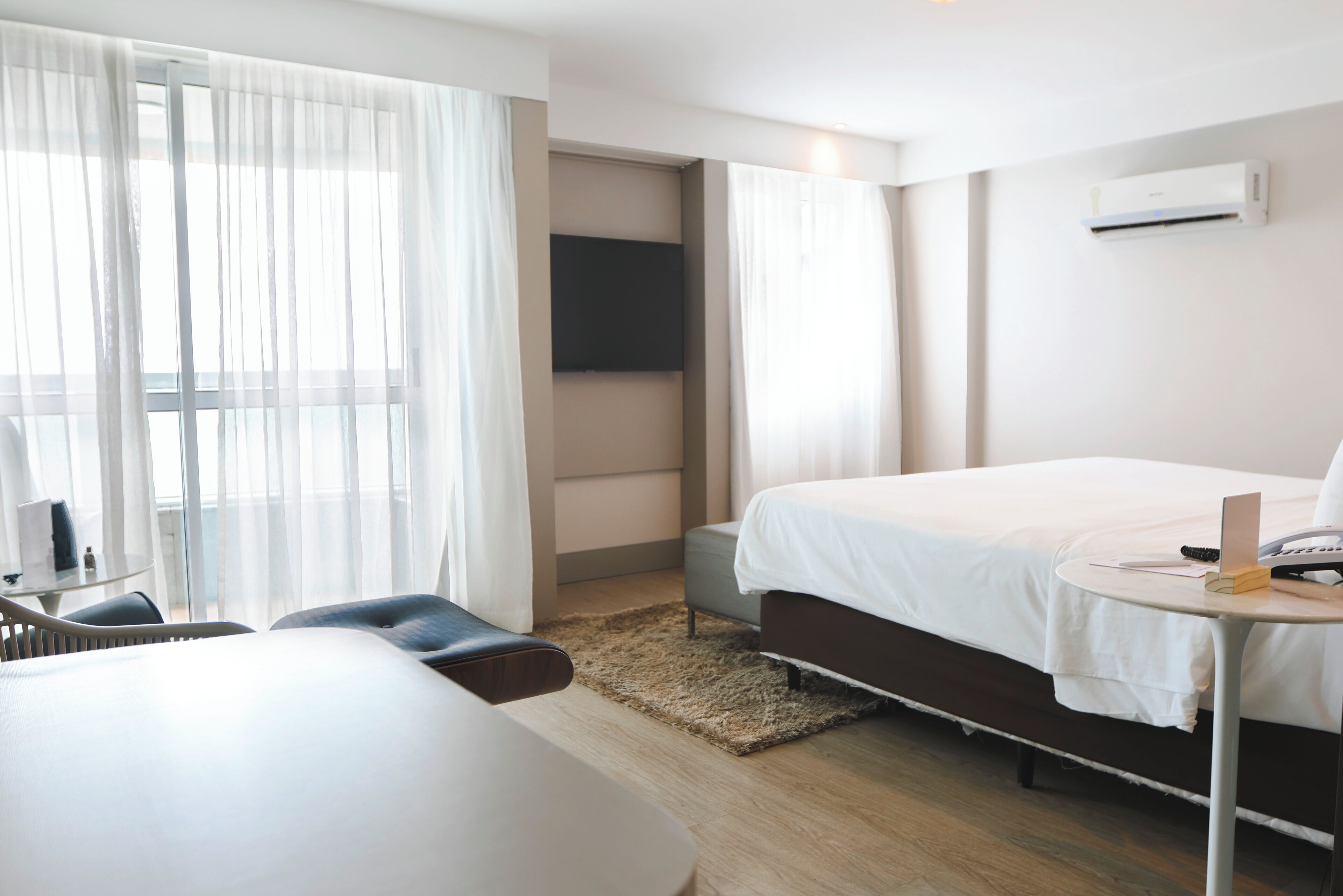 Ett modernt hotellrum med en säng, ett skrivbord, en stol och en tv som är monterad på väggen.
