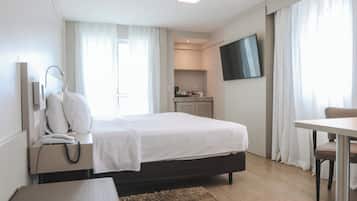 A hotel room with a bed, bedside table, lamp, phone, TV, and a small kitchenette area.