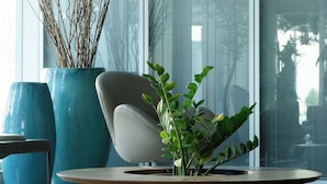 A modern interior with a round wooden coffee table, a white chair, and large blue planters with branches and green plants. - Radisson Hotel Recife (Recife)