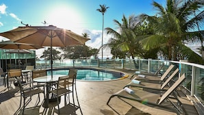 A poolside area with lounge chairs, umbrellas, and a glass-enclosed pool. - Radisson Hotel Recife (Recife)