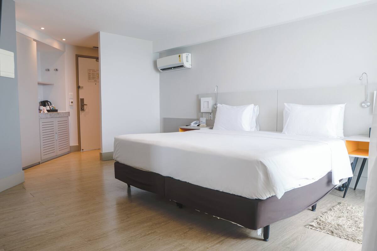 Ein modernes Hotelzimmer mit einem großen Bett, einem Nachttisch, einer Klimaanlage und Holzboden.