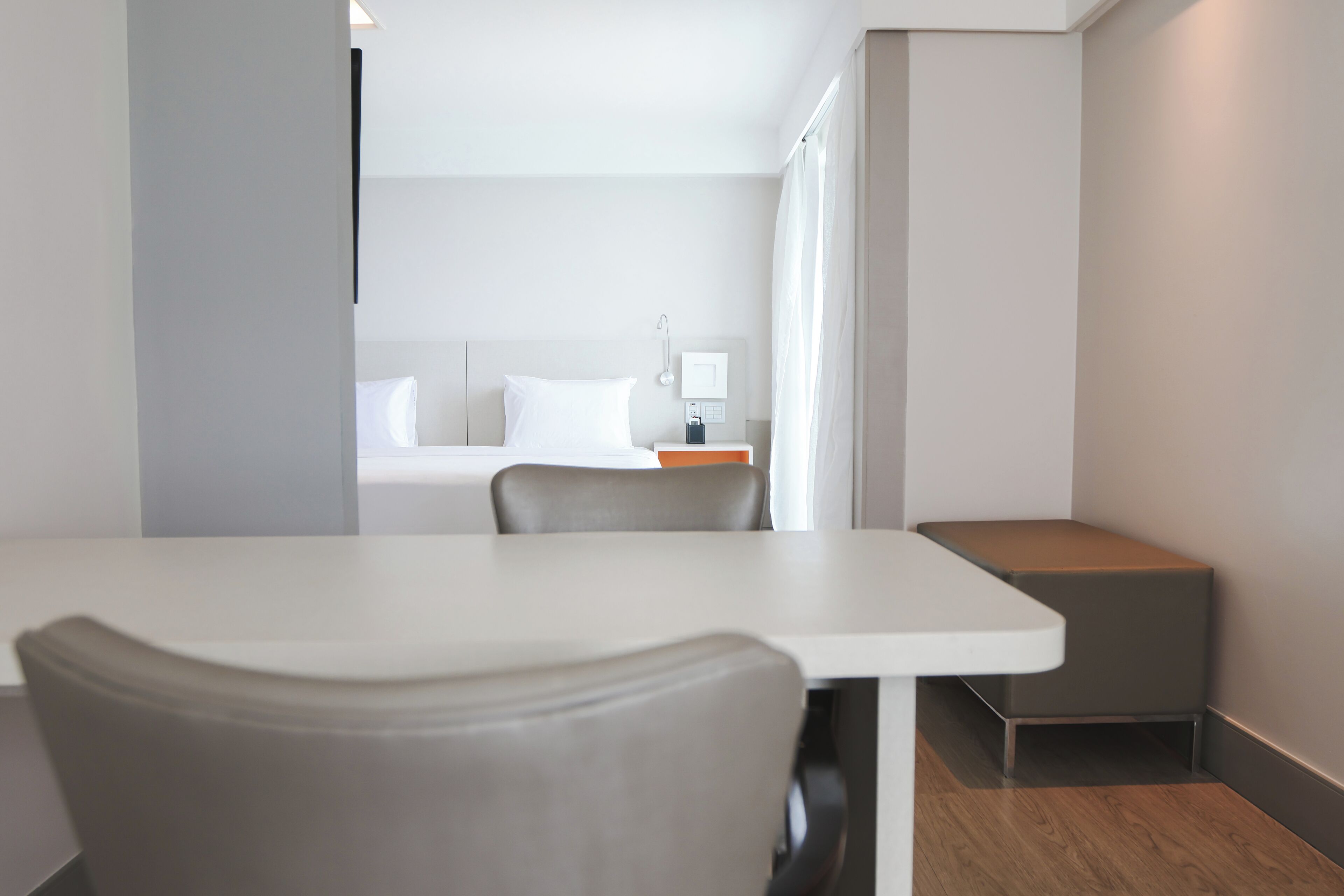 Une chambre d’hôtel moderne avec un lit blanc, une petite table, une chaise et une table de chevet avec une lampe.