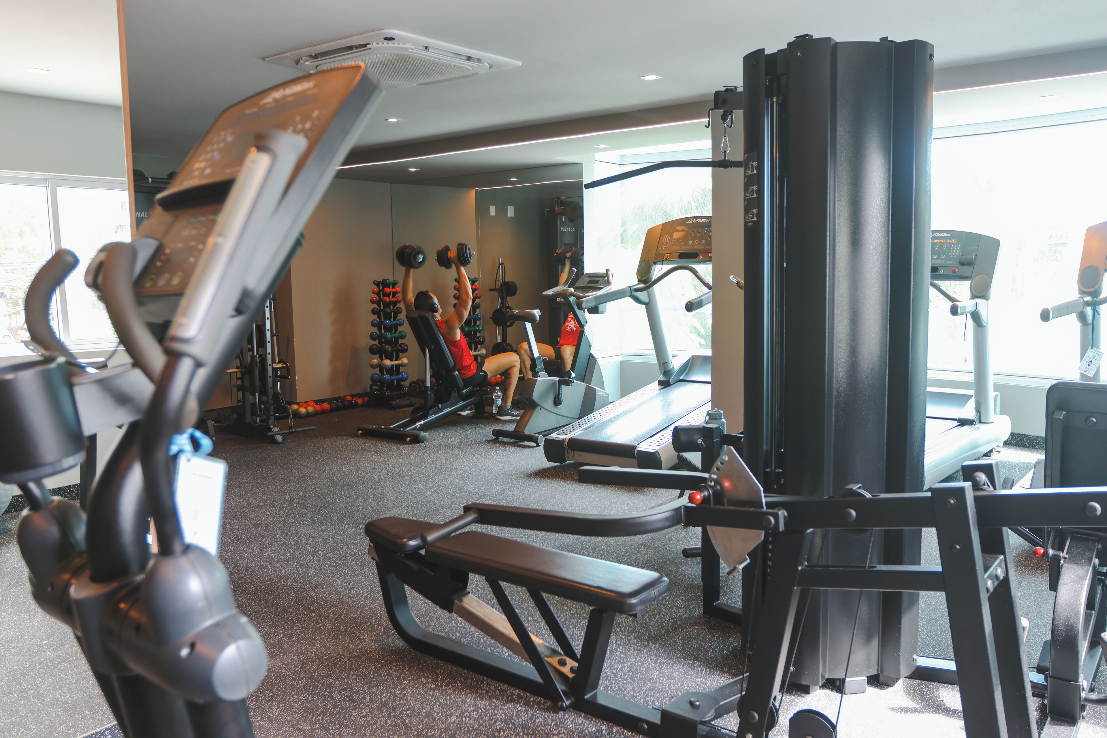 Un gimnasio con equipo de ejercicio variado, incluyendo cintas de correr, máquinas de pesas y mancuernas.