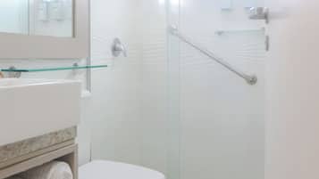 Een moderne badkamer met een douchecabine van glas, een wit toilet, een glazen plankje met toiletartikelen en een grote spiegel.