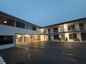A multi-story motel with a central courtyard, outdoor seating, and a covered parking area.