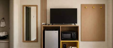 A hotel room with a flat-screen TV, a mini-fridge, a microwave, and a small coffee maker on a wooden shelf.
