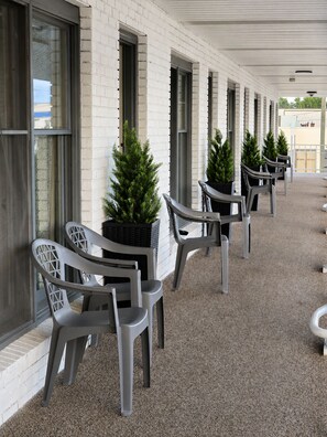 A covered outdoor seating area with plastic chairs and potted plants.