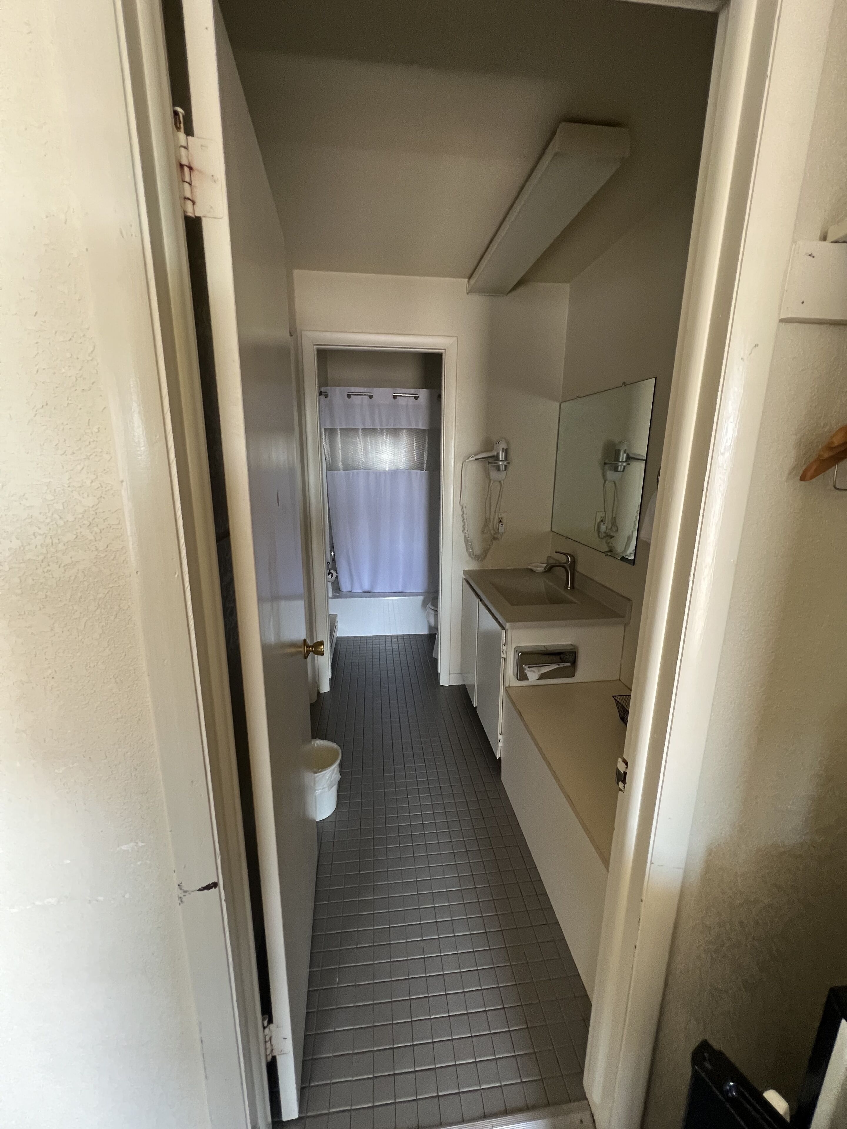 Un pasillo estrecho que conduce a un baño con ducha, inodoro y lavabo.