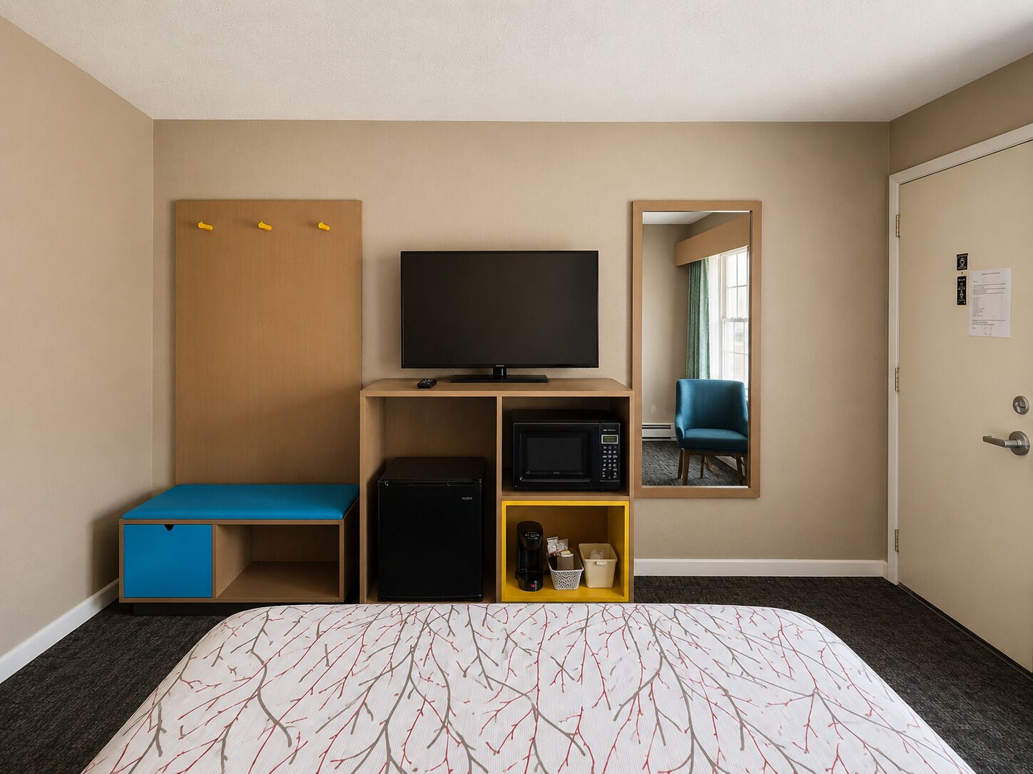 A hotel room with a bed, a television, a microwave, a small refrigerator, a desk with a chair, and a mirror.