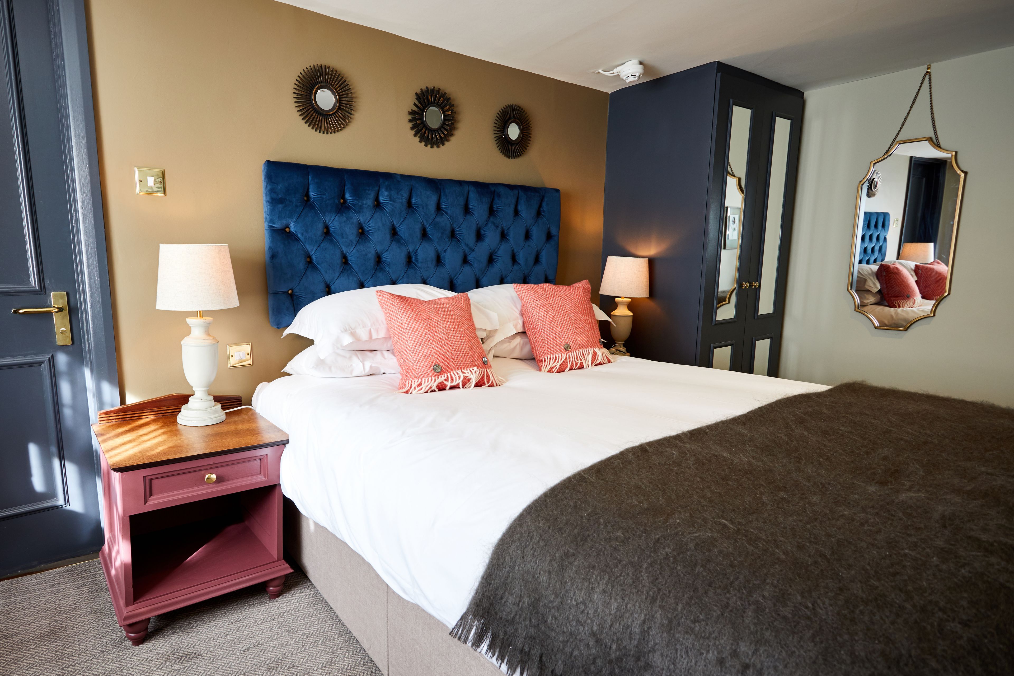 A bedroom with a large bed, two bedside tables, a mirror, and wall decorations.