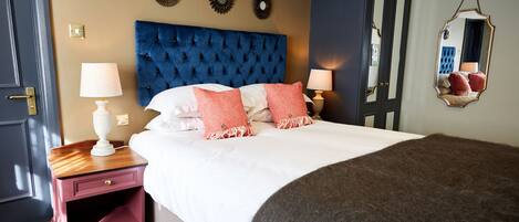 A bedroom with a large bed, two bedside tables, a mirror, and wall decorations.