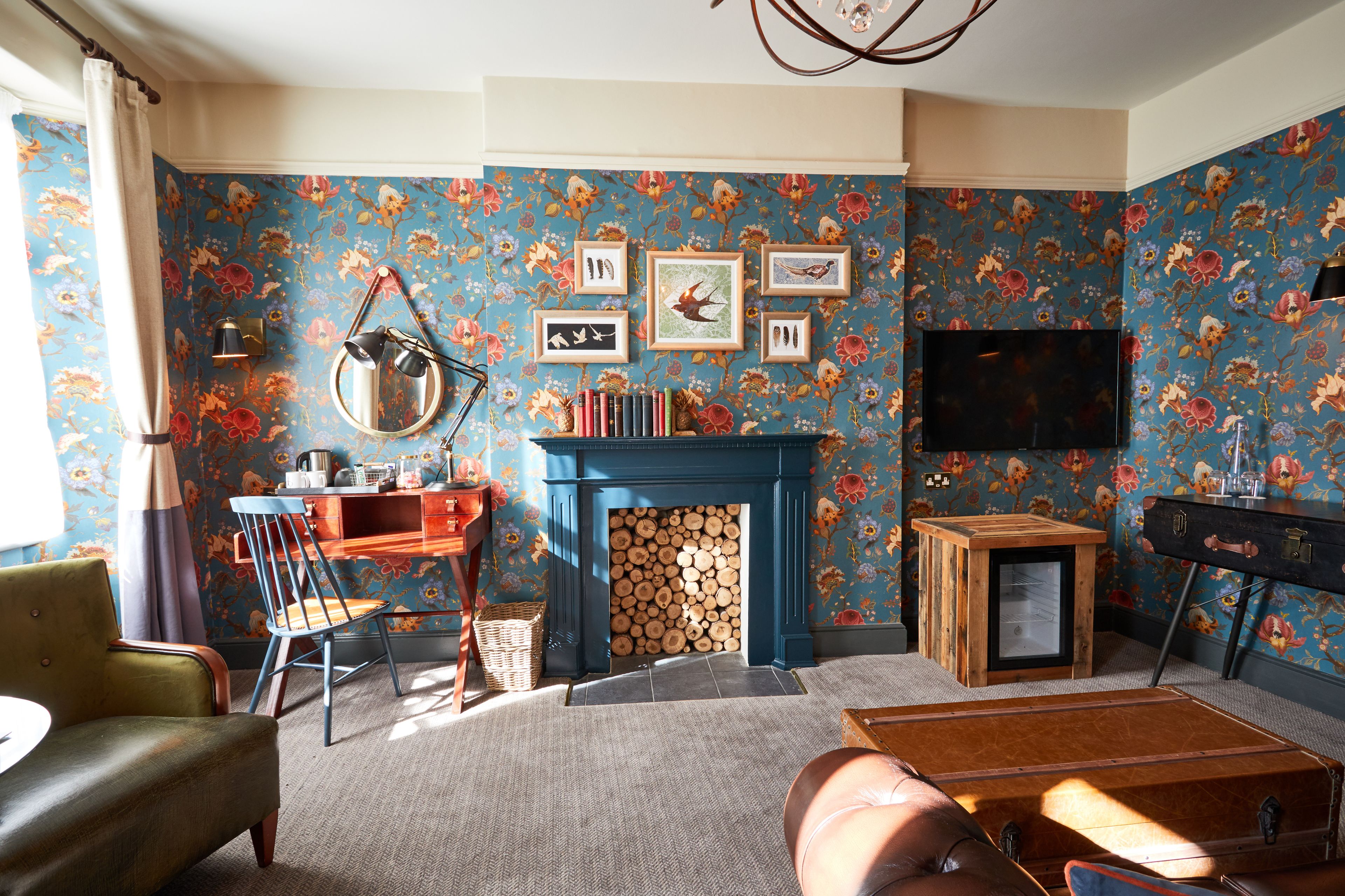 A living room with a fireplace, a television, and a floral wallpaper.
