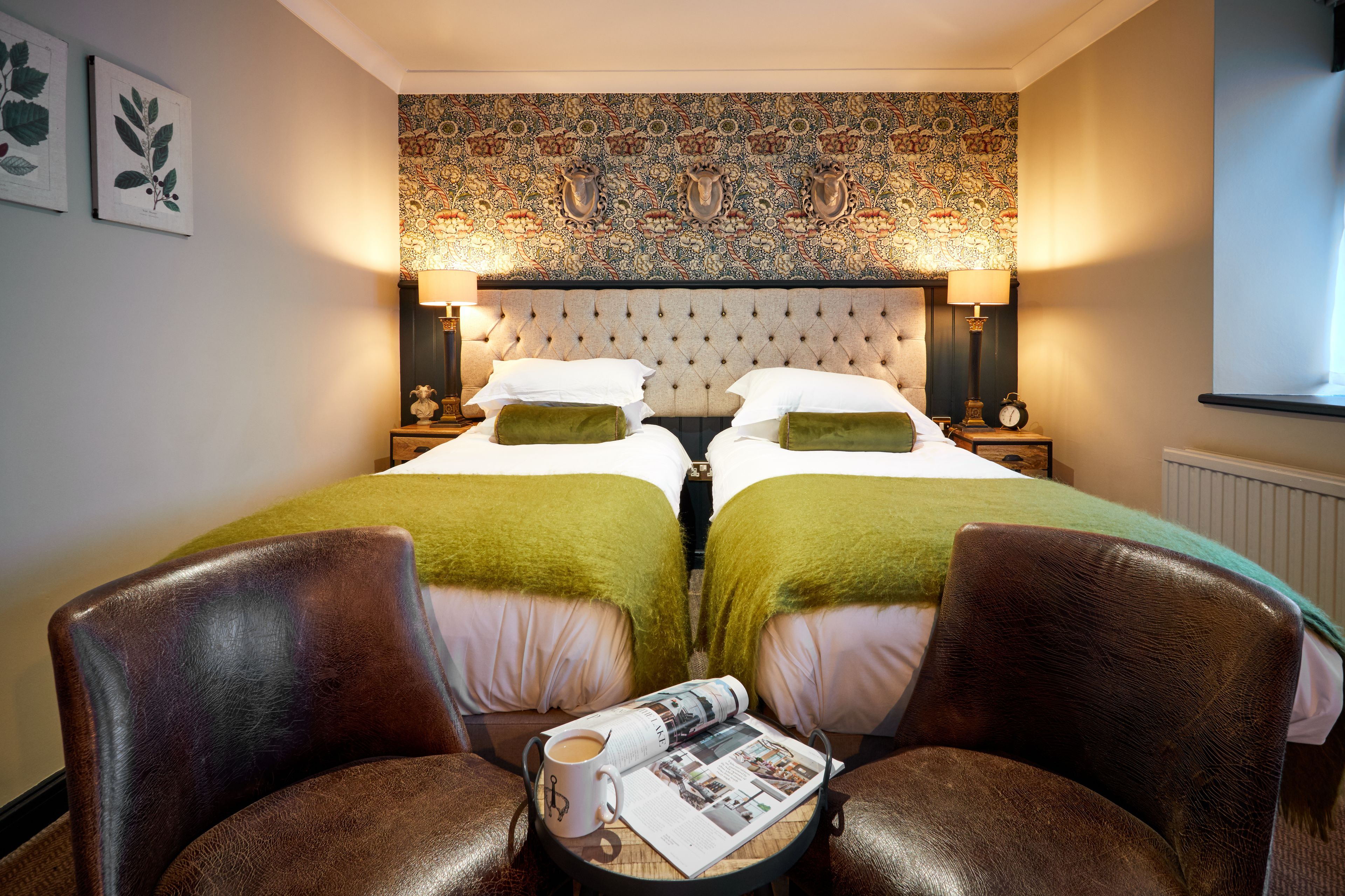Ein Hotelzimmer mit einem großen Bett, zwei Nachttischen, einem Tisch mit Zeitschrift und Tasse sowie zwei Ledersesseln.