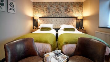 Ein Hotelzimmer mit einem großen Bett, zwei Nachttischen, einem Tisch mit Zeitschrift und Tasse sowie zwei Ledersesseln.