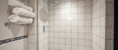 A shower area with a glass door, a towel rack with folded towels, and patterned tiles on the walls.