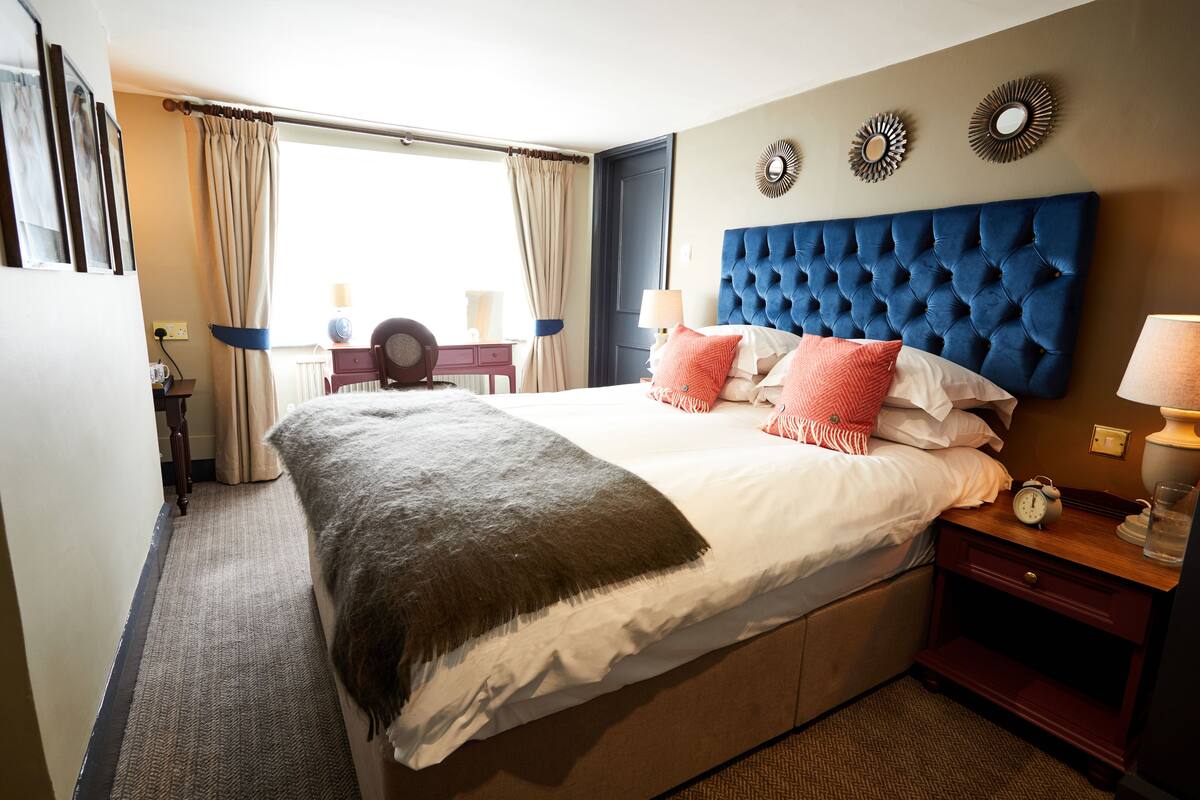 A hotel room with a large bed, a headboard, a nightstand, a lamp, and a view of the outdoors.