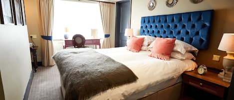 Ein Hotelzimmer mit einem großen Bett, einem Kopfteil, einem Nachttisch, einer Lampe und Blick ins Freie.