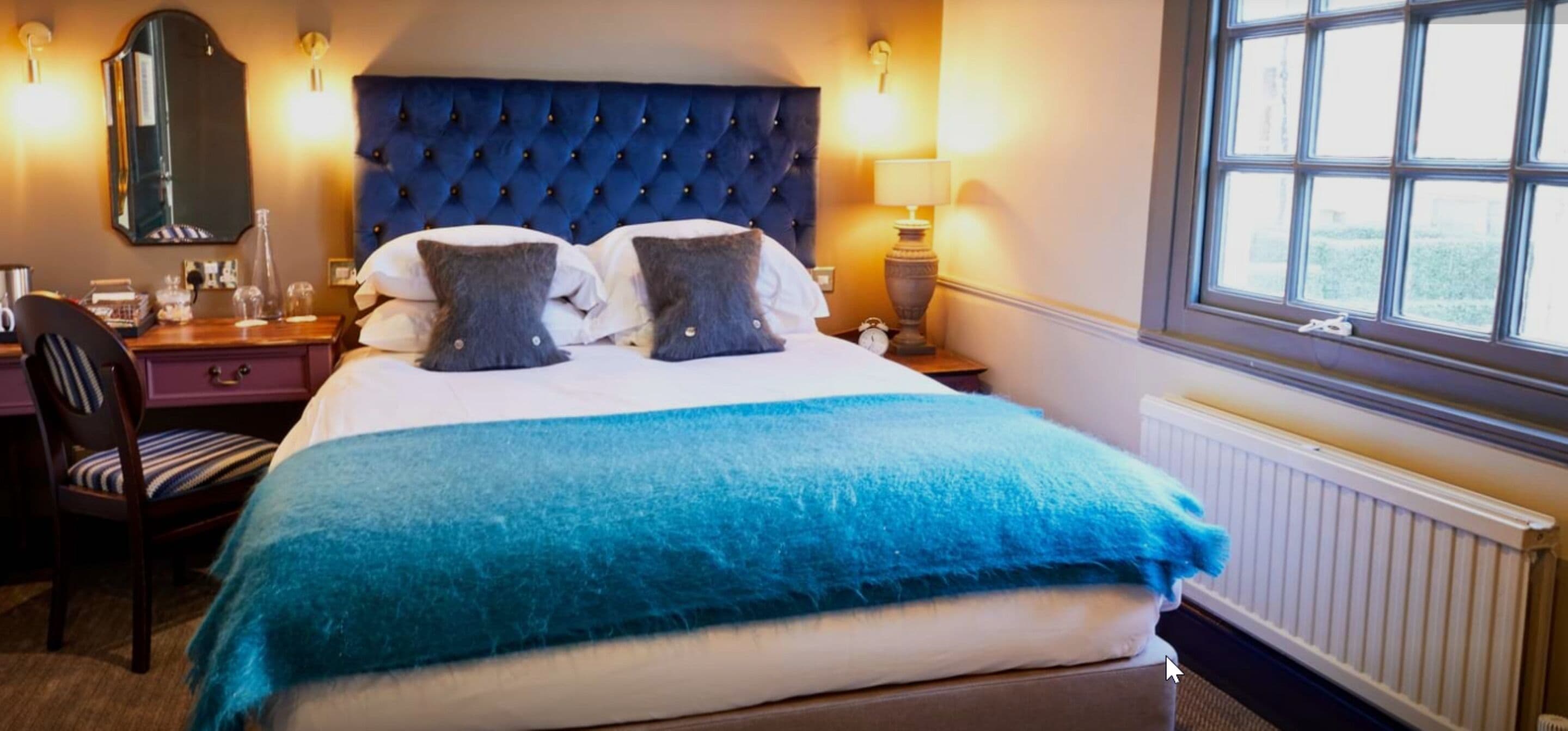 A hotel room with a large bed, a headboard, bedside lamps, a chair, a desk, and a window.
