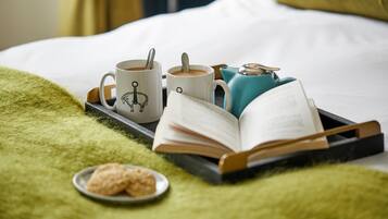 A bed with a green blanket, a tray with two mugs, a book, and a plate with cookies.