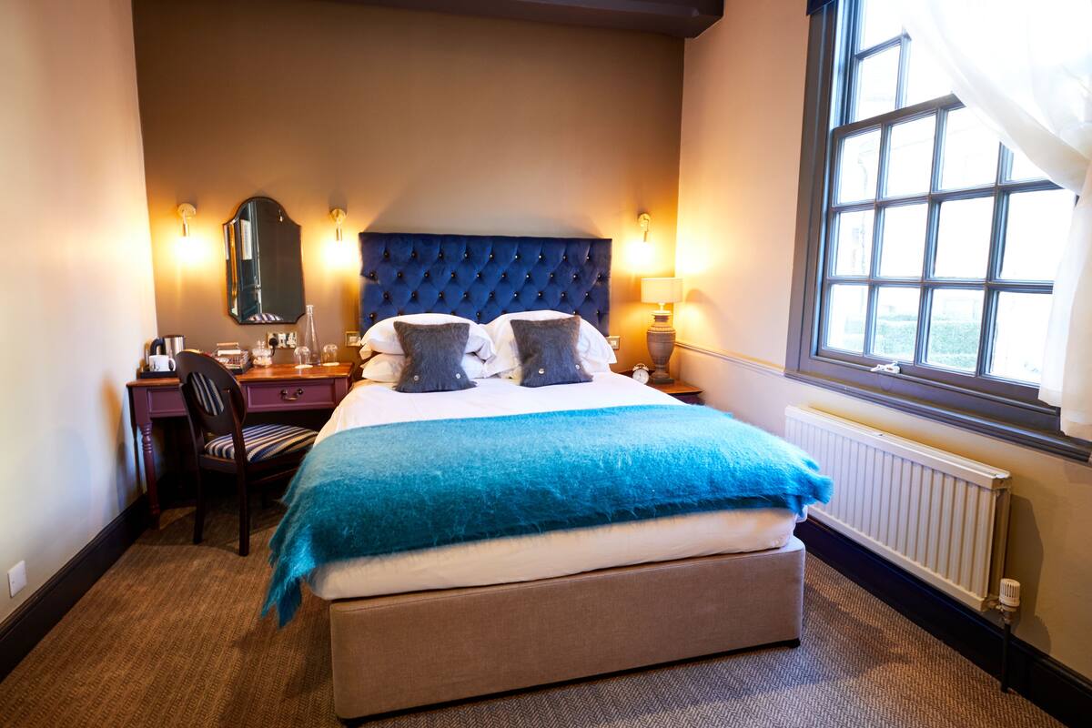 A hotel room with a large bed, a desk, a chair, a mirror, and a window with curtains.