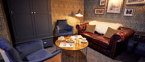 A cozy room with a dark wooden wardrobe, a blue armchair, a red leather sofa, and a round coffee table with a lamp.