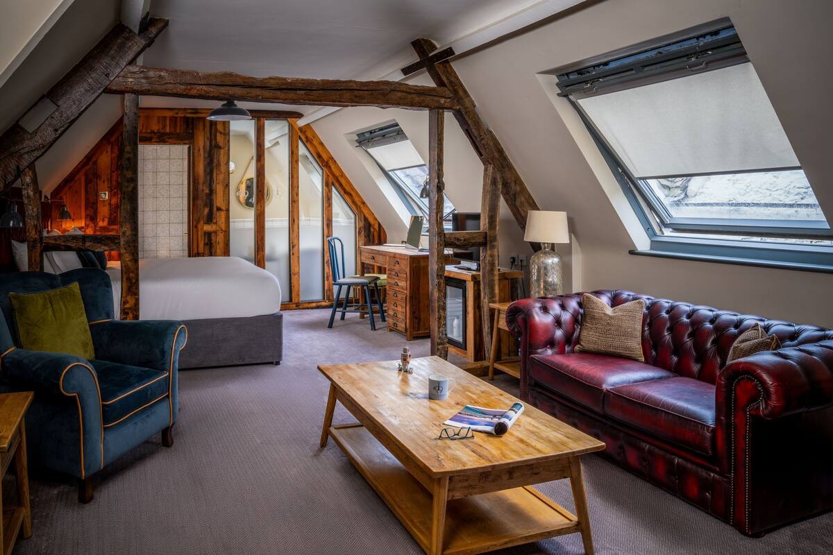 A loft-style room with a bed, a red leather sofa, a wooden coffee table, and a desk with a lamp.