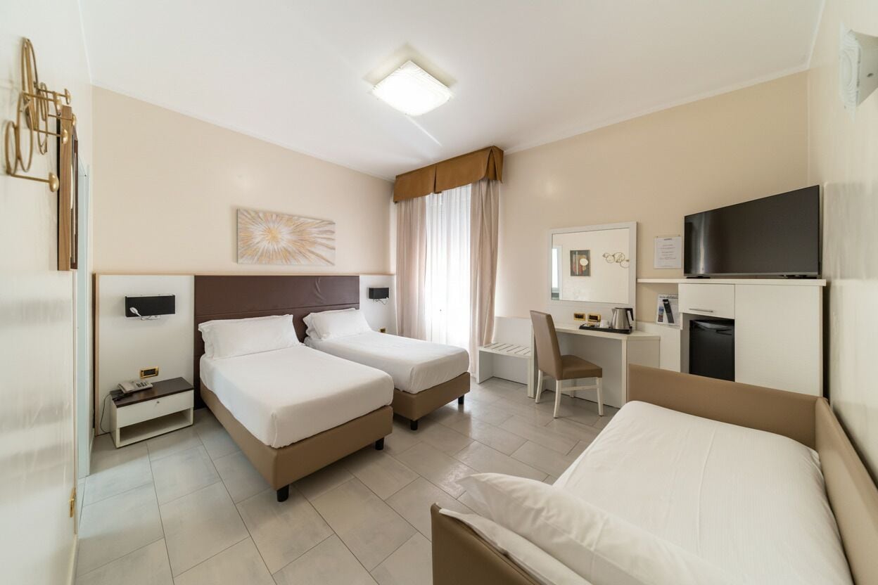 Camera d'albergo con due letti, una scrivania, una sedia, una televisione e un piccolo armadietto.