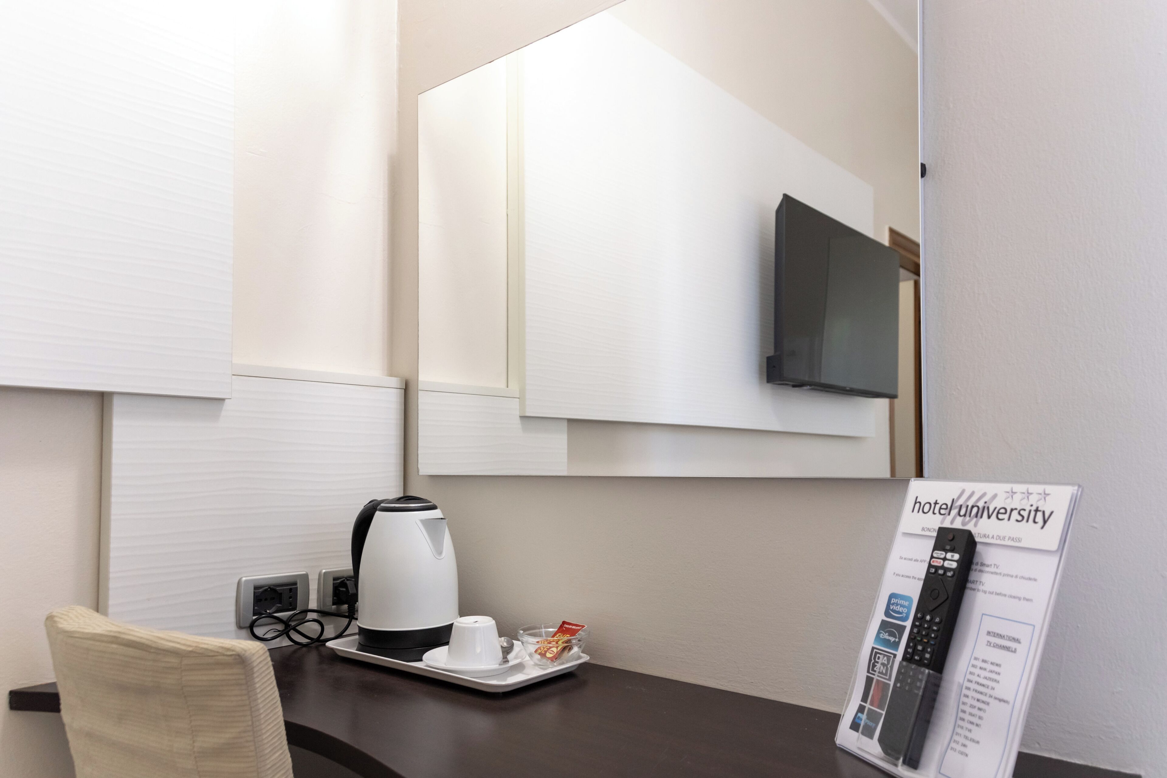 A hotel room with a coffee maker, a tray with a cup and snacks, a remote control, and a television mounted on the wall.